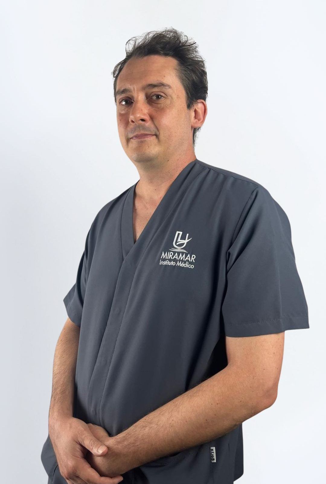 Dr Jose Losilla Dr. José Losilla, médico de Instituto Médico Miramar, retrato de tres cuartos con uniforme sanitario gris con el logo del centro