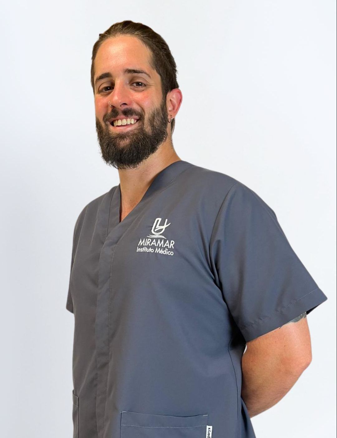 Dr. Álvaro Jofré Dr. Álvaro Jofré, especialista en Capilar de Instituto Médico Miramar, sonriendo con uniforme gris del centro, barba y pendiente